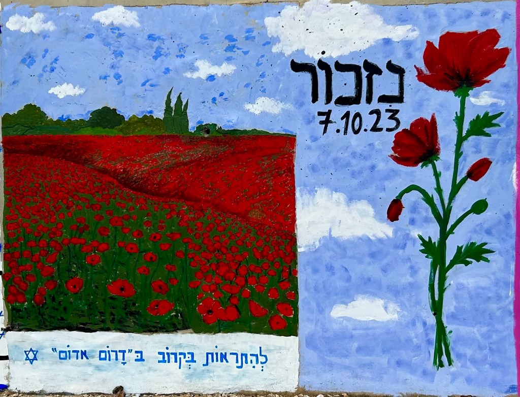 Ein Graffiti aus zwei Hälften, links ein Feld mit roten Blumen vor blauem Himmel, darunter hebräische Schrift, rechts eine einzelne rote Blume und ein hebräischer Schriftzug und das Datum 7.10.23