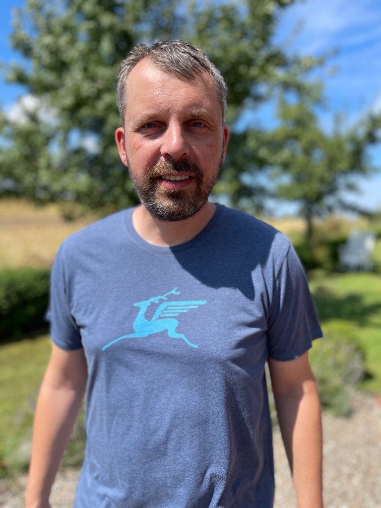 Foto von mir mit einem blauen Shirt, das ein hellblaues Huftier mit Flügeln zeigt.